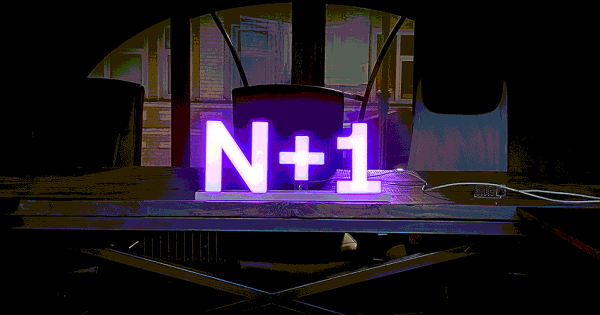 Светящийся логотип "N+1" на столе в тёмной комнате-сцене, фиолетовая подсветка.