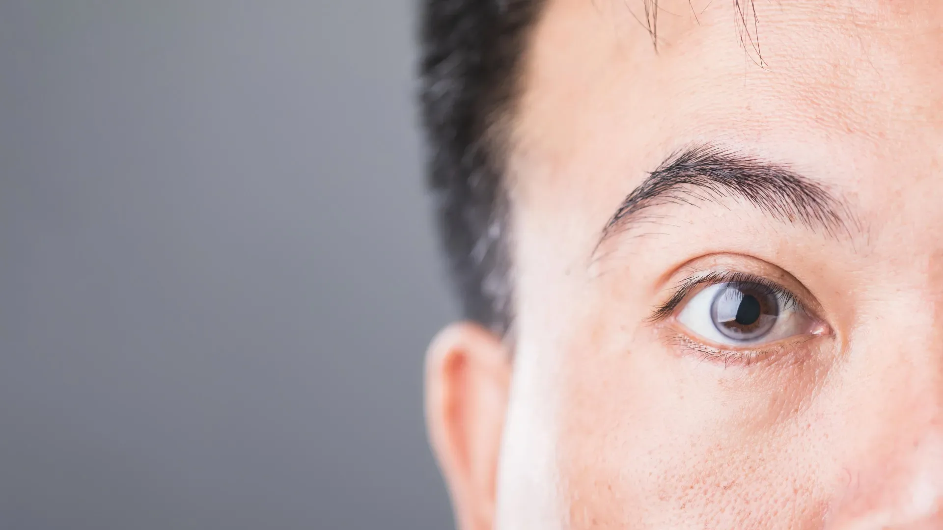 Фрагмент изображения человека с чёрными волосами на сером фоне.