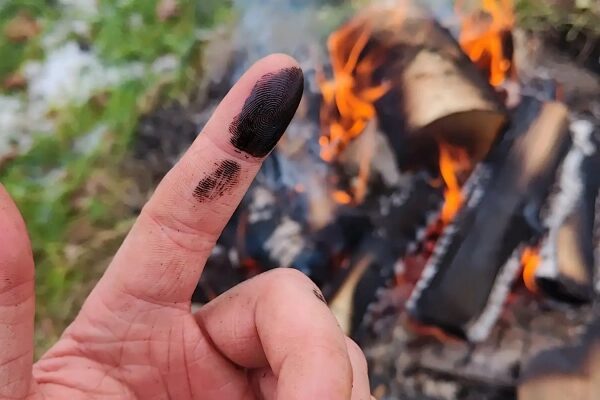 Палец с сажей на фоне костра в лесу.