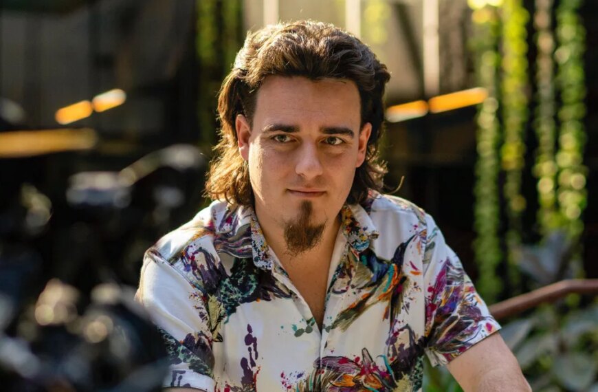 Мужчина в яркой рубашке сидит в саду, солнечный свет падает на волосы и одежду.