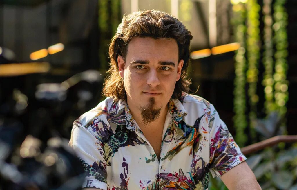 Мужчина в яркой рубашке сидит в саду, солнечный свет падает на волосы и одежду.