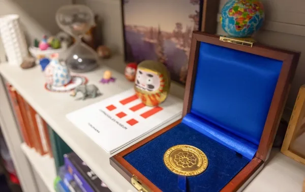 Фотография полок в кабинете Кэрри Парч, на которых размещены различные книги и безделушки, а также плоский золотой медальон в деревянном футляре, обитом синей тканью.