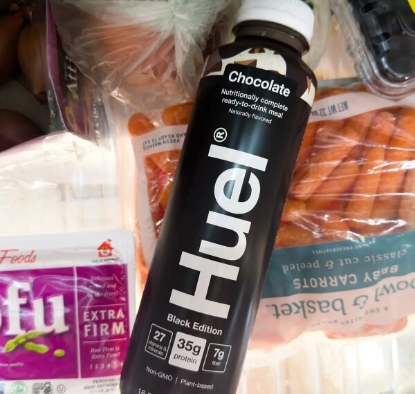 Бутылка шоколадного напитка Huel на фоне продуктов в холодильнике.