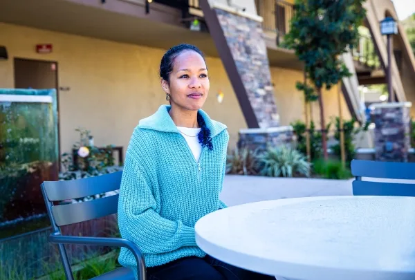 Женщина в синем свитере сидит за столиком на улице.