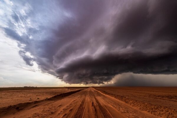 Гроза над полем с грунтовой дорогой, темные облака нависают низко над землей.
