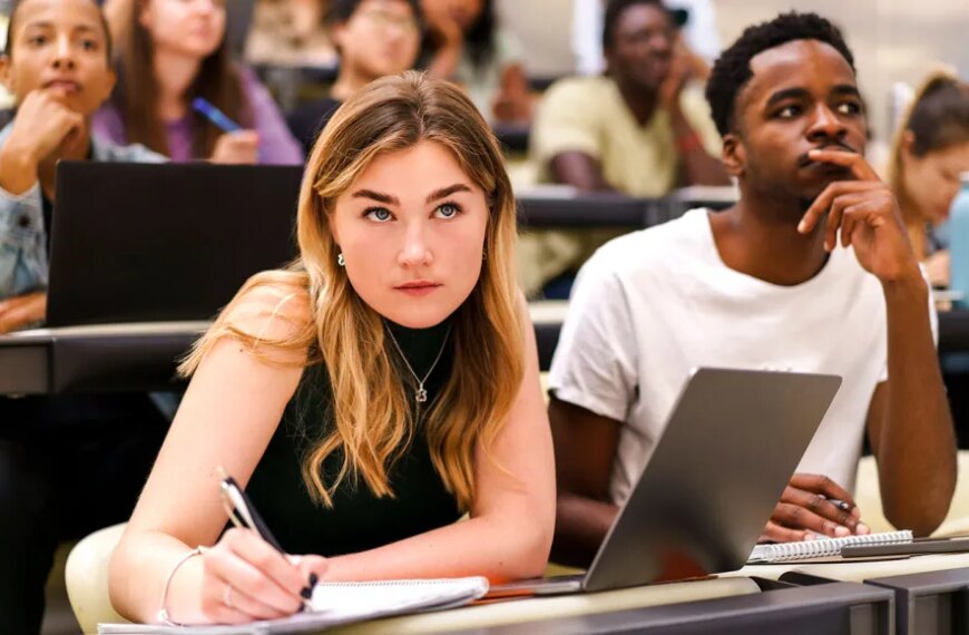 Студенты в аудитории с ноутбуками и тетрадями, занимаются на лекции в университете.