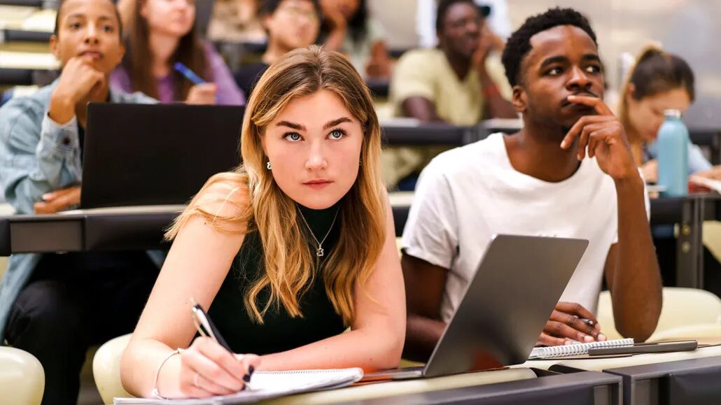 Студенты в аудитории с ноутбуками и тетрадями, занимаются на лекции в университете.