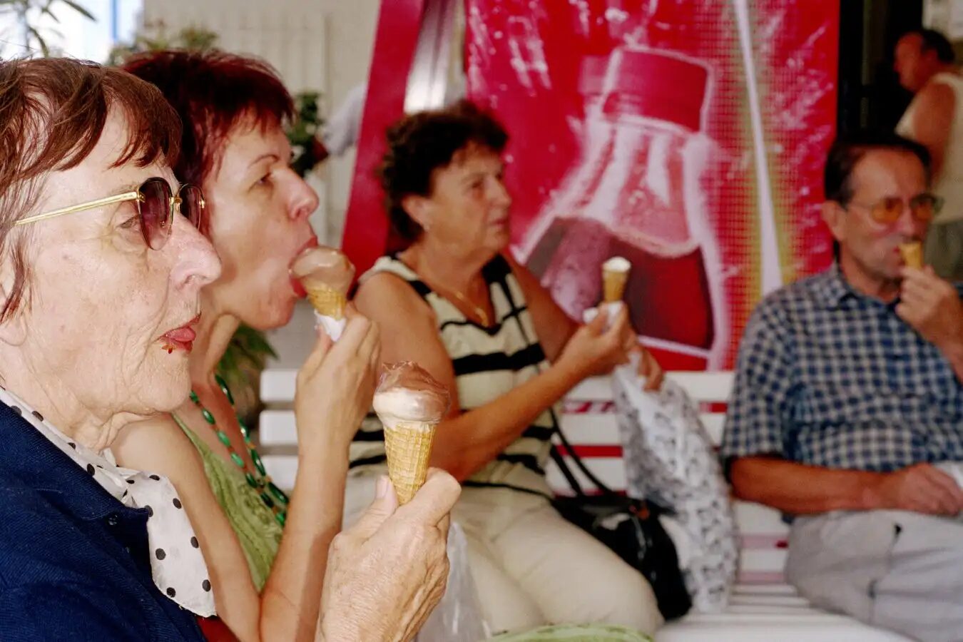 Люди сидят на скамейке и едят мороженое на фоне рекламы напитка.