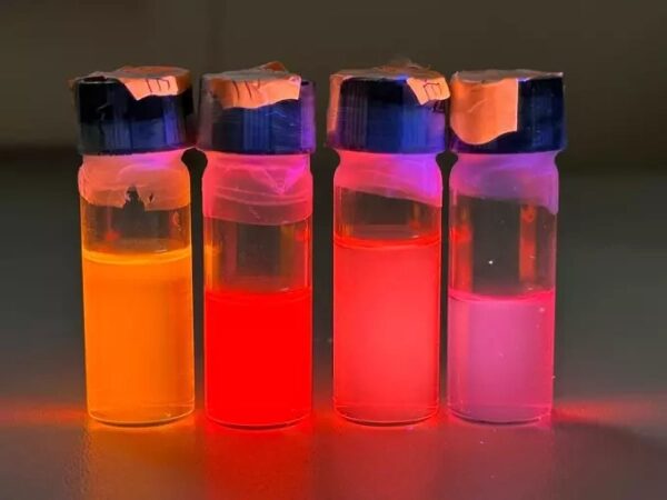 Четыре флакона с яркими флуоресцентными жидкостями под ультрафиолетовым светом.
