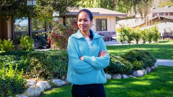 Человек в голубом свитере стоит на зелёной лужайке перед домом в солнечный день.