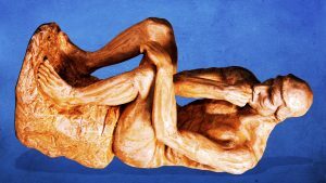 Деревянная скульптура человека в задумчивой позе на синем фоне.