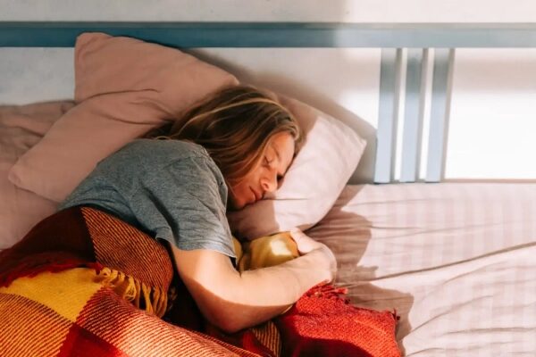 Человек спит в кровати под красным пледом, солнечный свет падает на подушку.