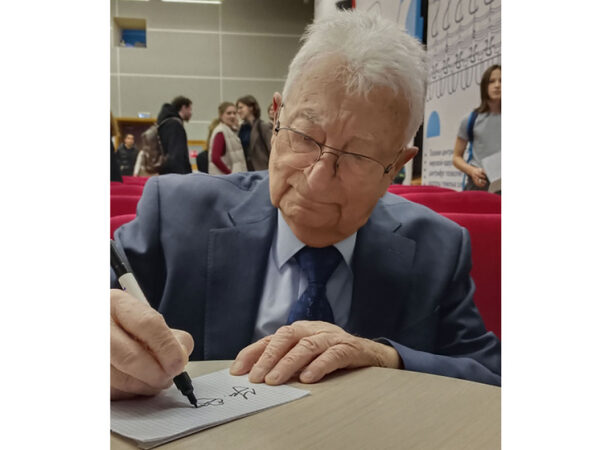 Академик Юрий Оганесян обсудил в МИФИ пределы существования материального мира 6 Человек в костюме подписывает автограф на мероприятии.