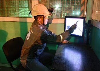 Рабочий в каске работает с монитором на промышленном объекте.