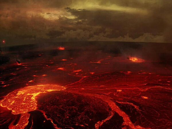 Извержение вулкана с потоками лавы и дымом на фоне темного неба.