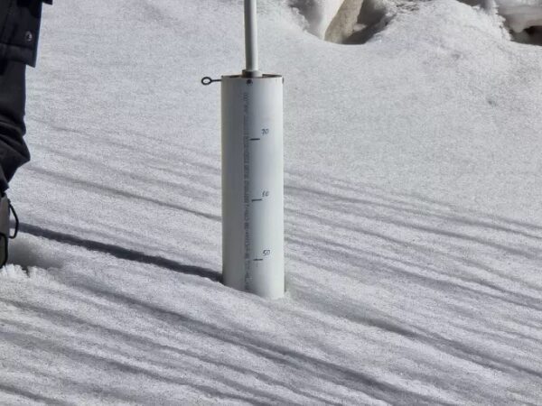 Снегомер в снегу показывает толщину снежного покрова на светлом фоне.