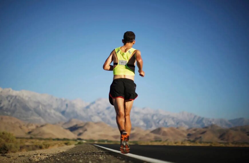 Бегун в яркой форме бежит по дороге с горным пейзажем на фоне.