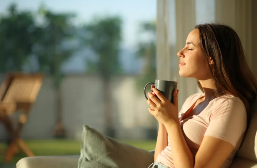 Женщина с чашкой чая сидит на диване, наслаждаясь утренним солнцем в гостиной.