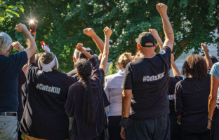 Группа людей на митинге, поднятые руки, футболки с надписью #CutsKill.