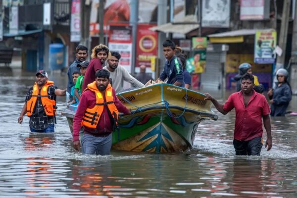Люди на лодке плывут по затопленной улице в жилетах безопасности.