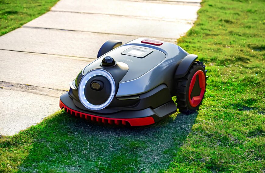Робот-газонокосилка на зеленом газоне рядом с тротуаром.