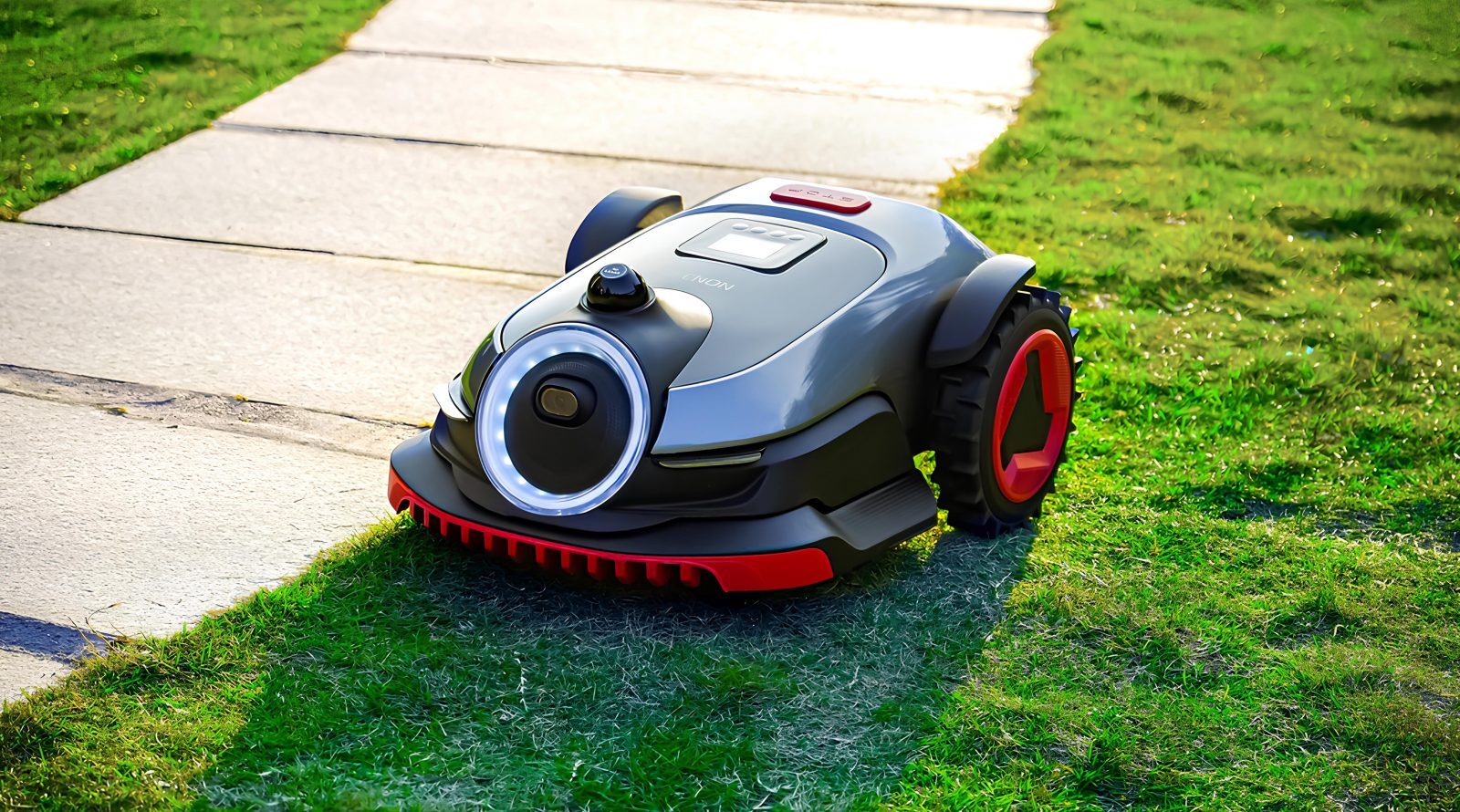 Робот-газонокосилка на зеленом газоне рядом с тротуаром.