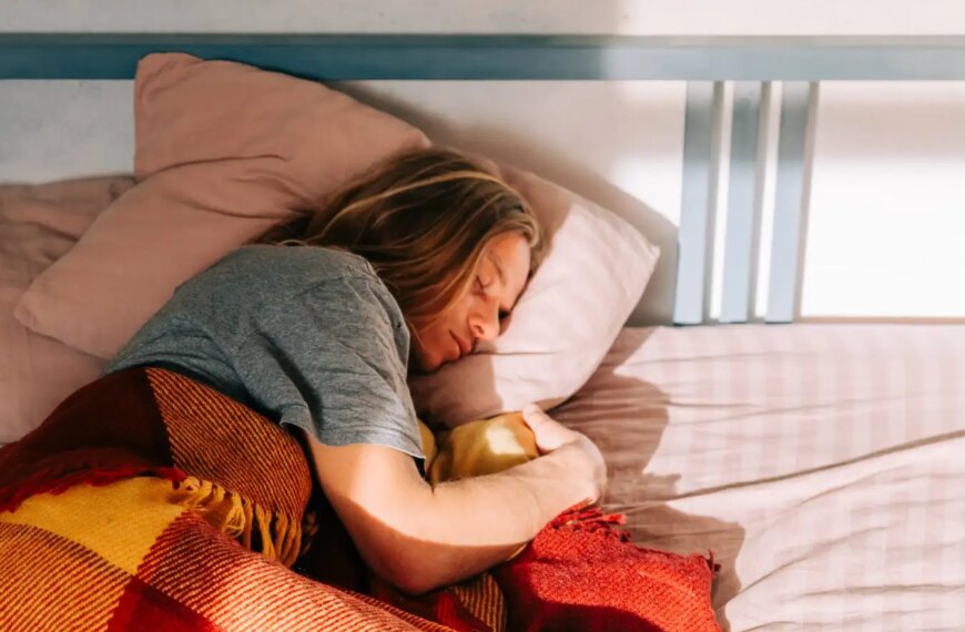 Человек отдыхает в кровати, накрытый одеялом, солнечный свет падает на постель.