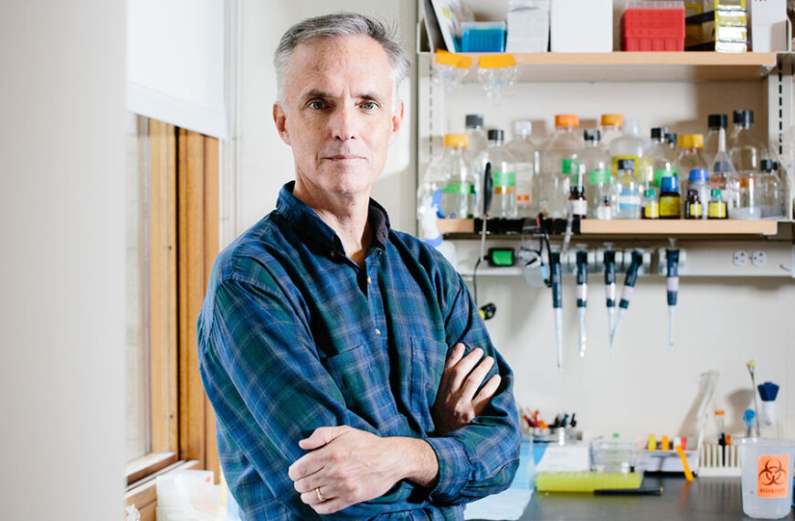 Человек в лаборатории. На фоне полки с лабораторными принадлежностями и приборами.