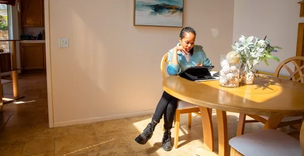 Женщина сидит за столом и смотрит в свой iPad.