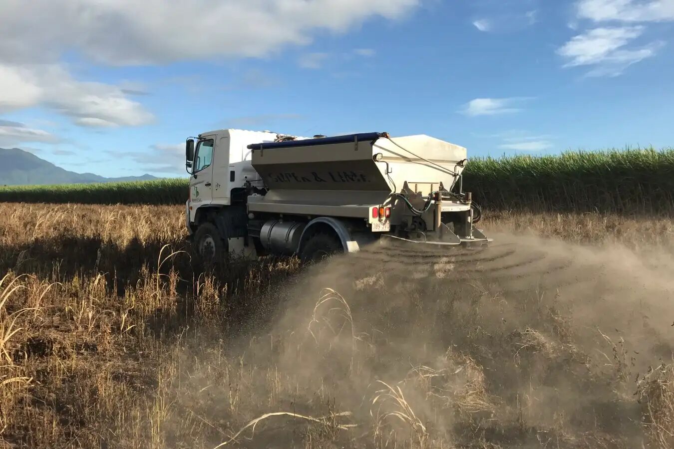 Грузовик разбрасывает удобрения на сельскохозяйственном поле под голубым небом.
