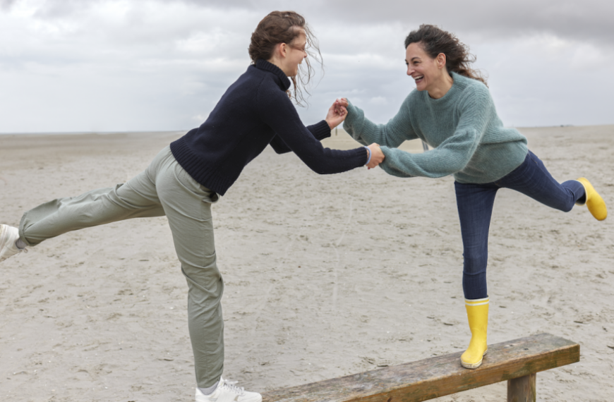 Две девушки в качестве упражнения балансируют на доске на пляже.