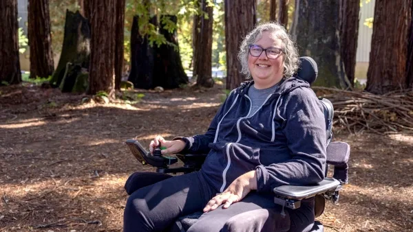 Человек в инвалидной коляске в лесу, окружённый большими деревьями.