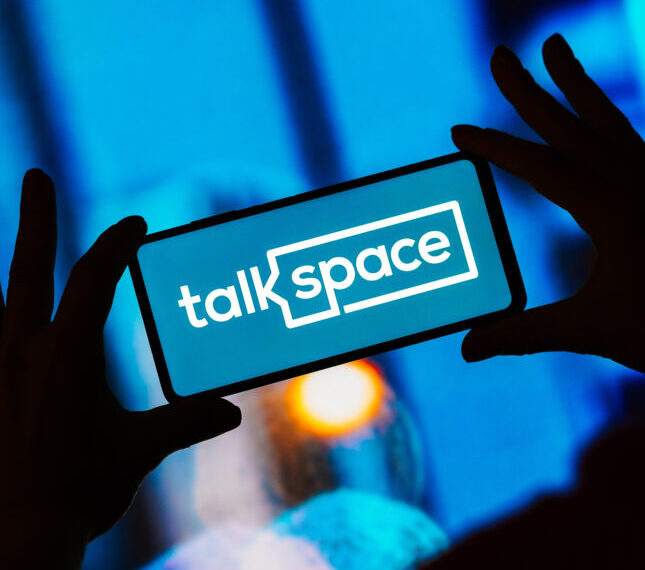 Смартфон с логотипом Talkspace на синем фоне в руках человека.