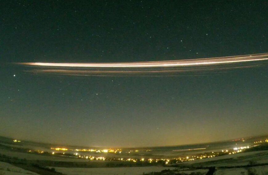 Яркая полоса от падающего метеора в ночном небе над городом, звезды и огни на фоне.