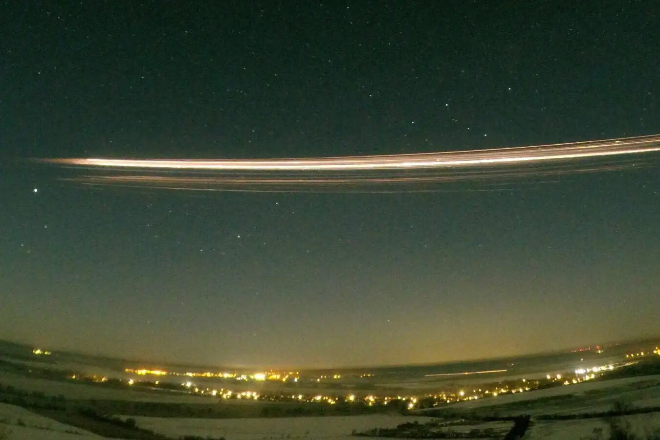 Яркая полоса от падающего метеора в ночном небе над городом, звезды и огни на фоне.