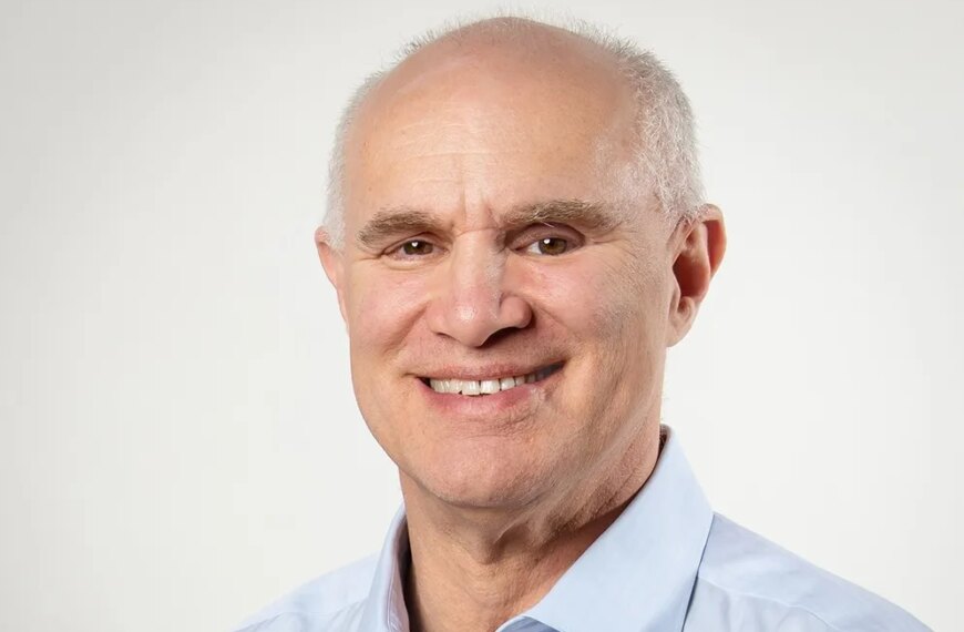 Портрет улыбающегося мужчины в светло-голубой рубашке на светлом фоне.