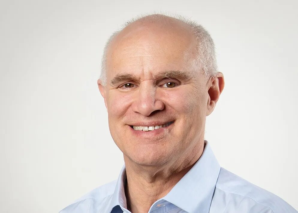 Портрет улыбающегося мужчины в светло-голубой рубашке на светлом фоне.