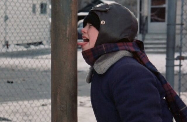 Человек в зимней одежде с языком на столбе, сцена на улице зимой.