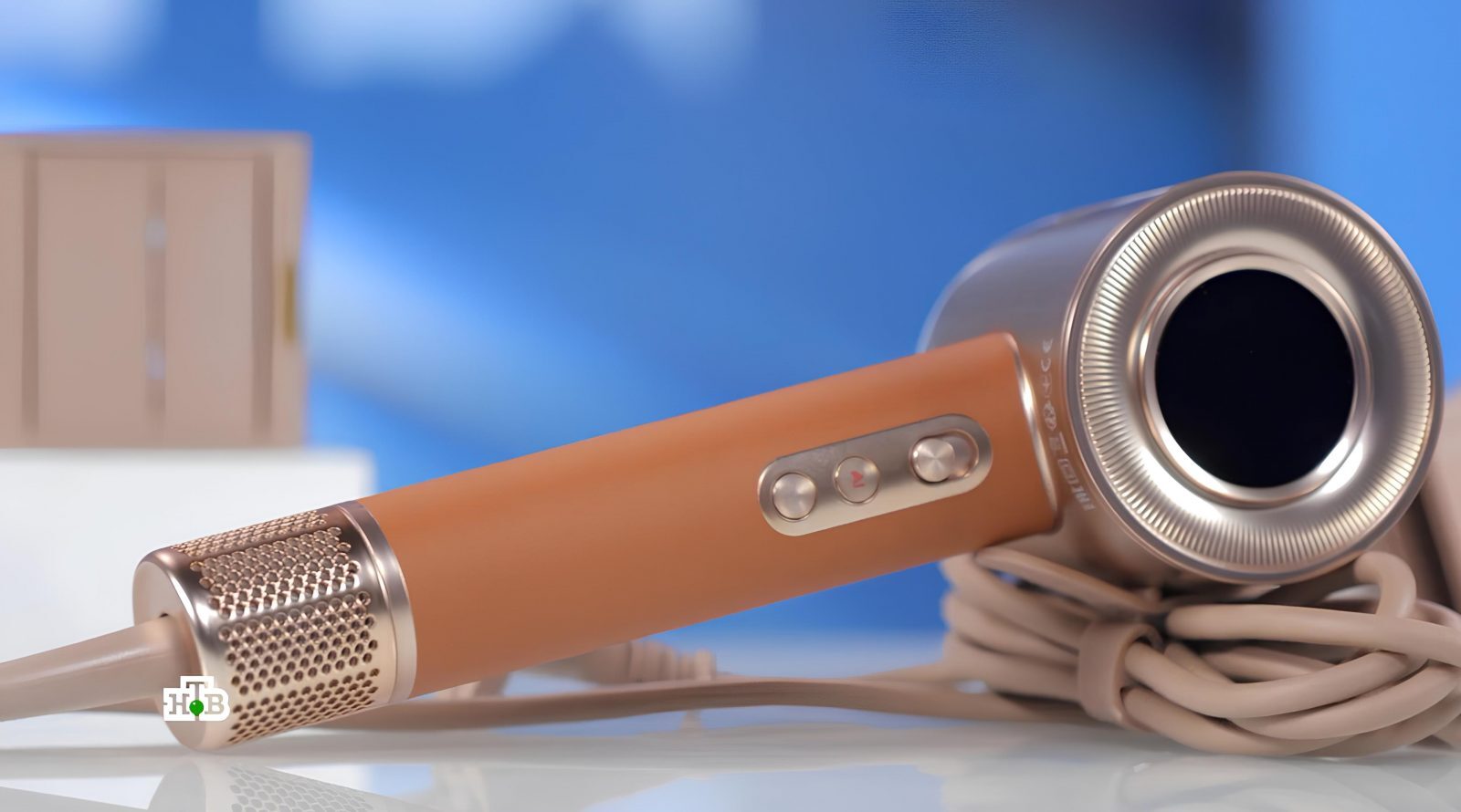 Фен с интеллектом и ароматизацией потока 2 Коричневый фен с кнопками управления на фоне голубого размытого фона.