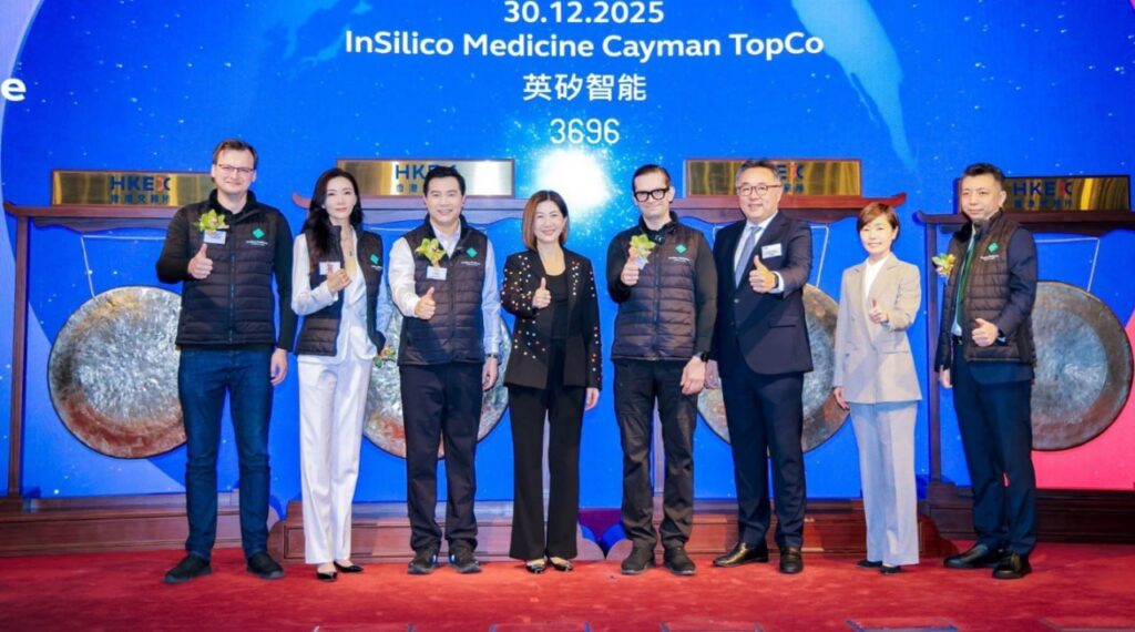 Группа людей в костюмах и жилетах улыбается и показывает жест "класс" на фоне баннера.