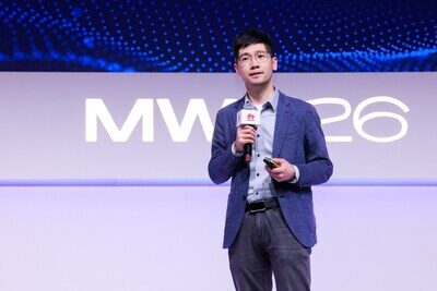 Человек в пиджаке выступает на фоне баннера MWC26 с микрофоном.