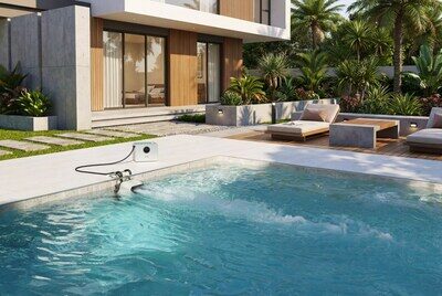 Современный бассейн в саду у дома с шезлонгами и зелеными растениями на заднем плане.