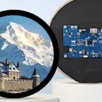 Круглый экран с изображением замка и горы, рядом электронная плата.