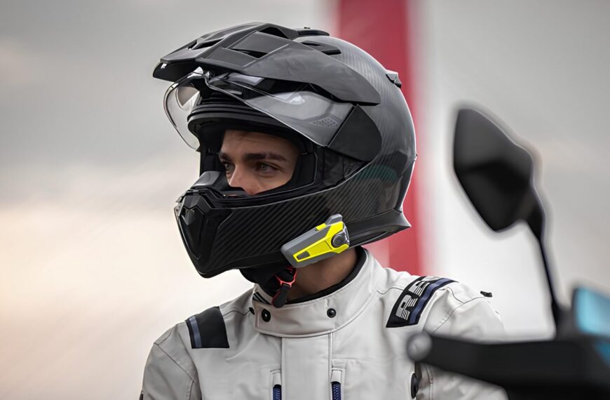 Мотоциклист в шлеме и защитной экипировке на фоне мотоцикла и моста.