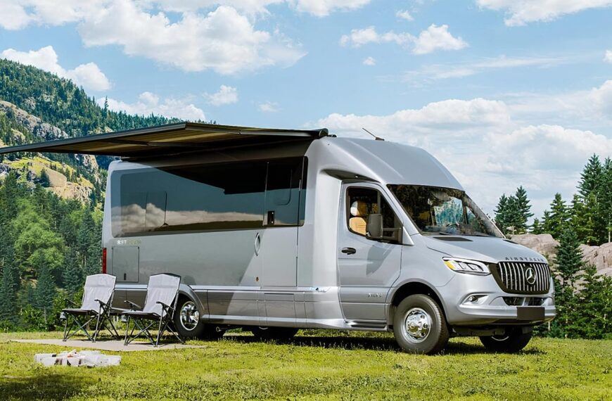 Дом на колесах в лесу с раскладными стульями и выдвижным тентом для кемпинга.