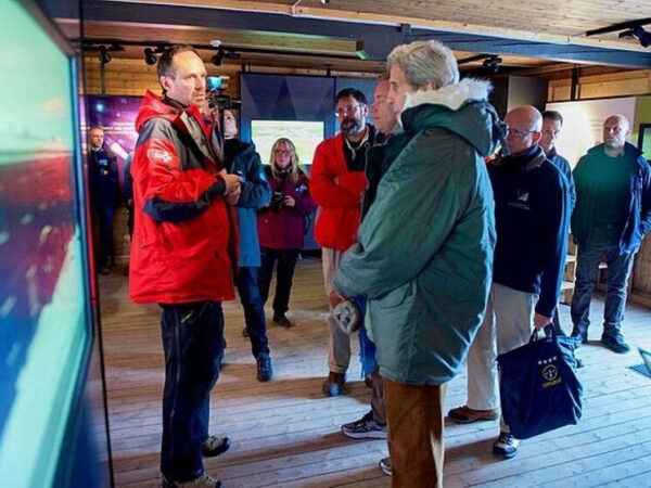 Группа людей в тёплой одежде слушает мужчину на презентации в деревянной комнате.