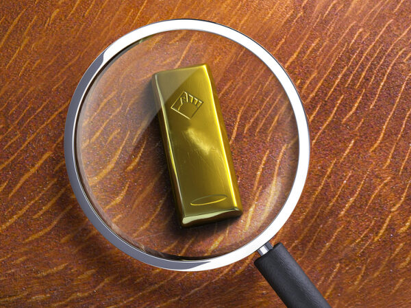 Золотой слиток под увеличительным стеклом на деревянном столе.