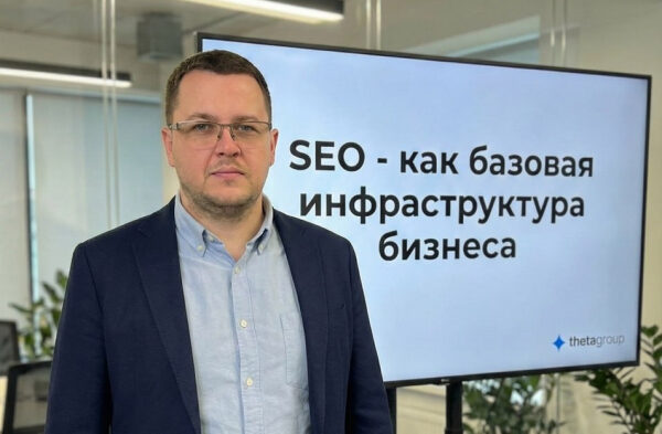 Мужчина в офисе рядом с экраном, на котором написано "SEO - как базовая инфраструктура бизнеса".