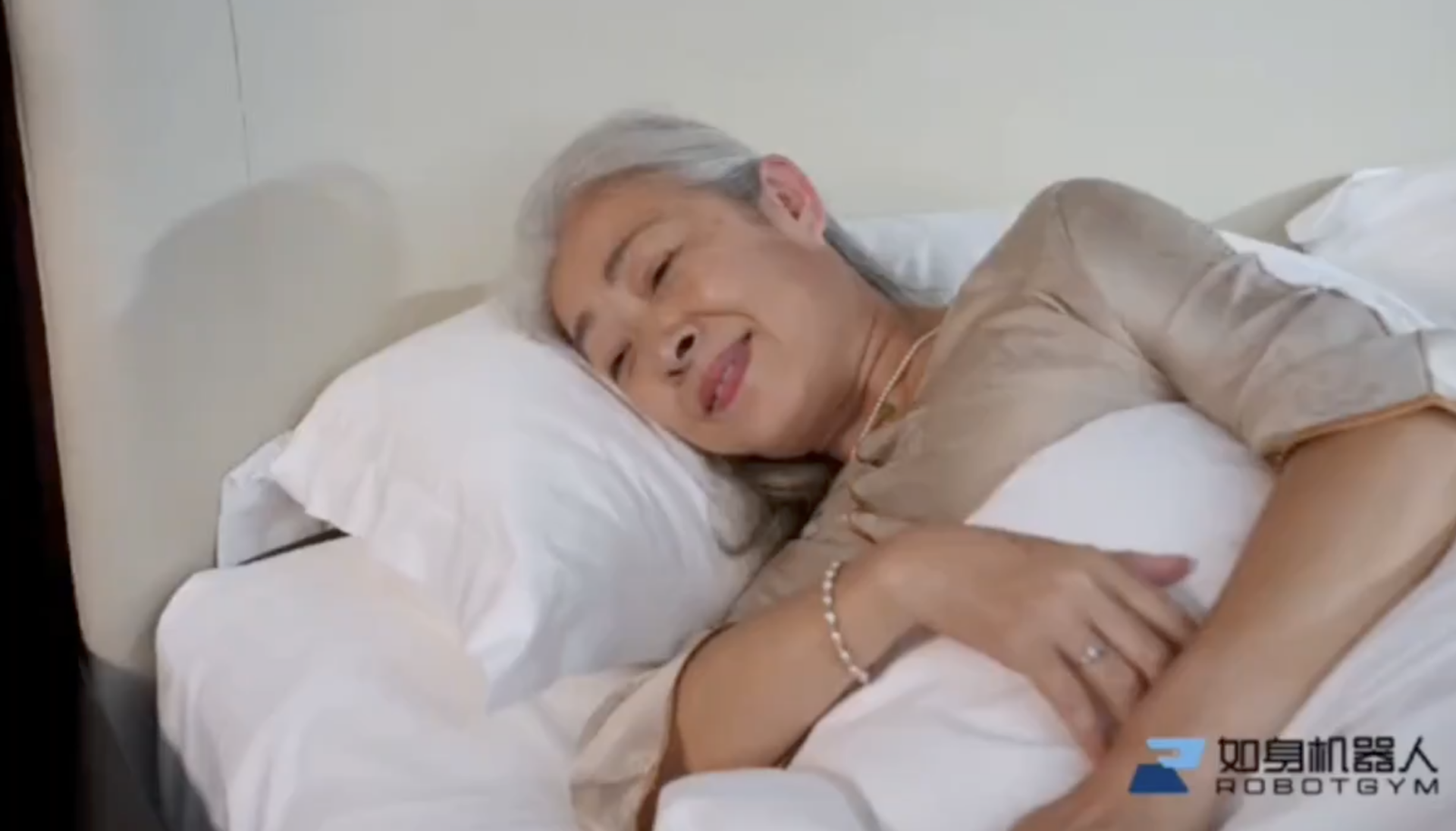 Пожилая женщина отдыхает в постели с улыбкой, лежа на белых подушках.