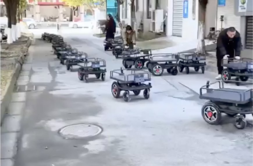 Роботы-курьеры на улице в ряд, люди управляют ими в городе.